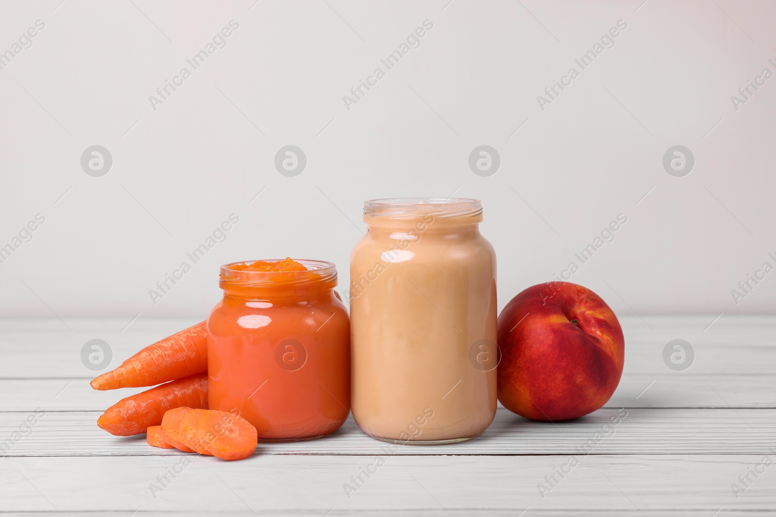 Photo of Jars of healthy baby food and ingredients on white wooden table, closeup