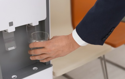 Photo of Man filling glass from water cooler indoors, closeup