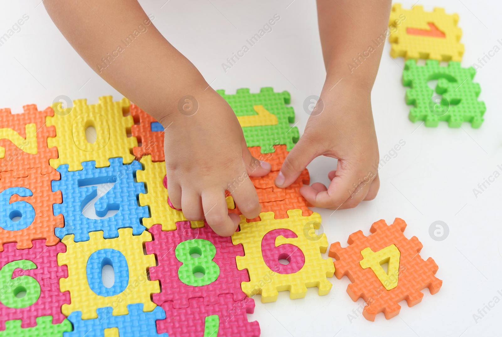 Photo of Little girl playing with colorful puzzles at white table, closeup. Educational toy