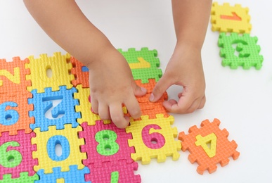 Little girl playing with colorful puzzles at white table, closeup. Educational toy