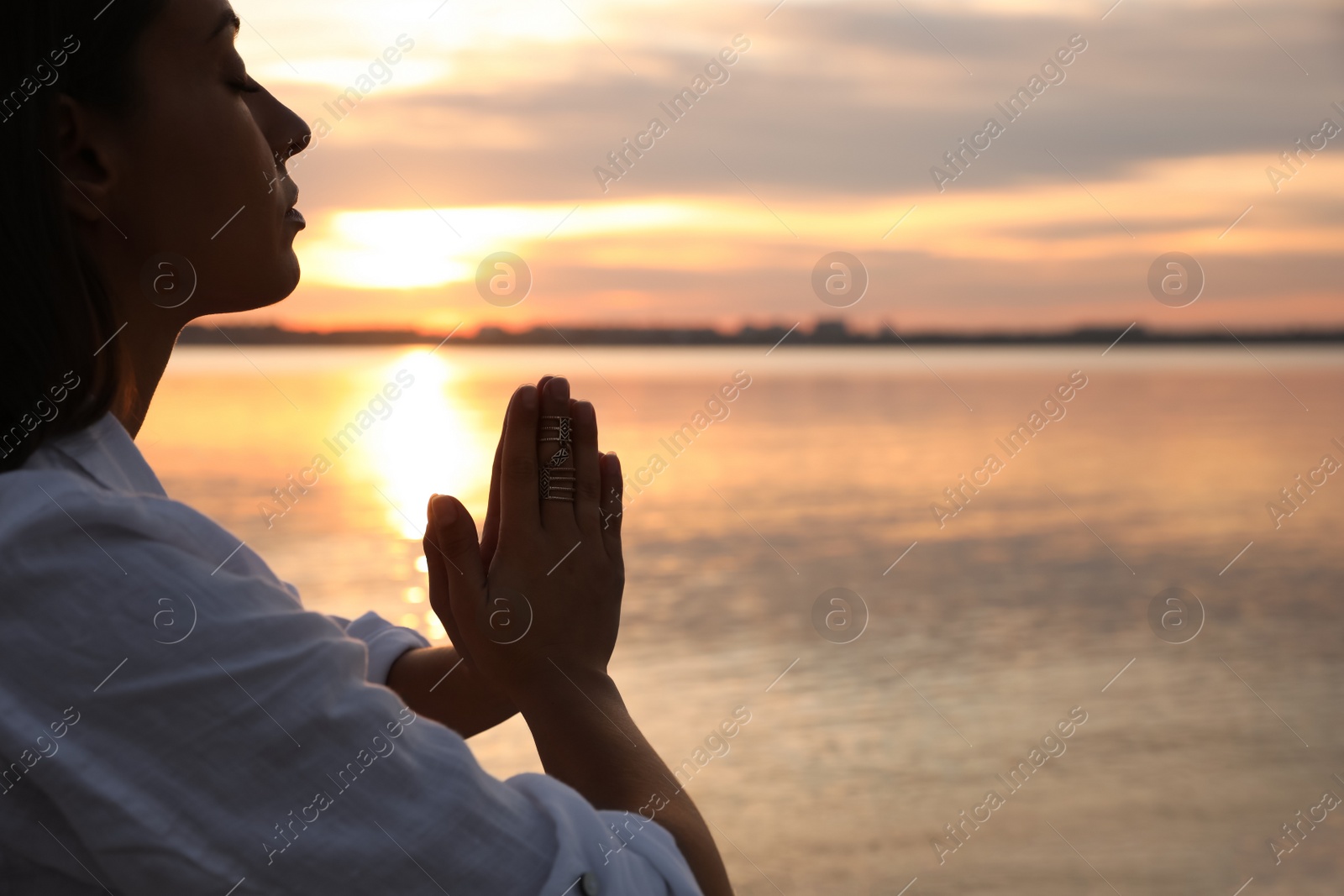 Photo of Young woman meditating near river at sunset, closeup view with space for text. Nature healing power