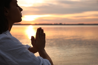 Photo of Young woman meditating near river at sunset, closeup view with space for text. Nature healing power