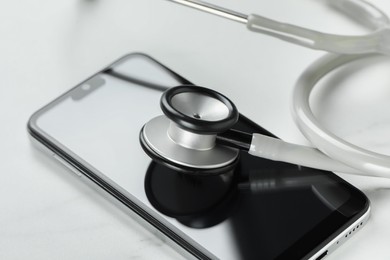 Photo of Modern smartphone and stethoscope on white table, closeup