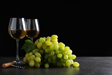 Photo of Fresh ripe juicy grapes with wineglasses on grey table against black background, space for text