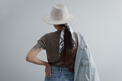 Young woman with hat and stylish bandana on light background, back view