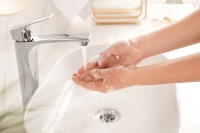 Photo of Young woman washing hands with soap over sink in bathroom, closeup