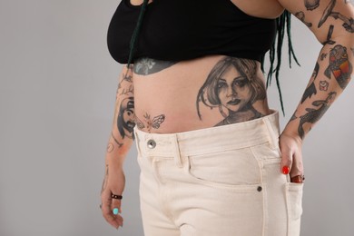 Woman with tattoos on body against grey background, closeup