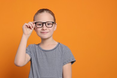 Photo of Portrait of cute girl in glasses on orange background. Space for text