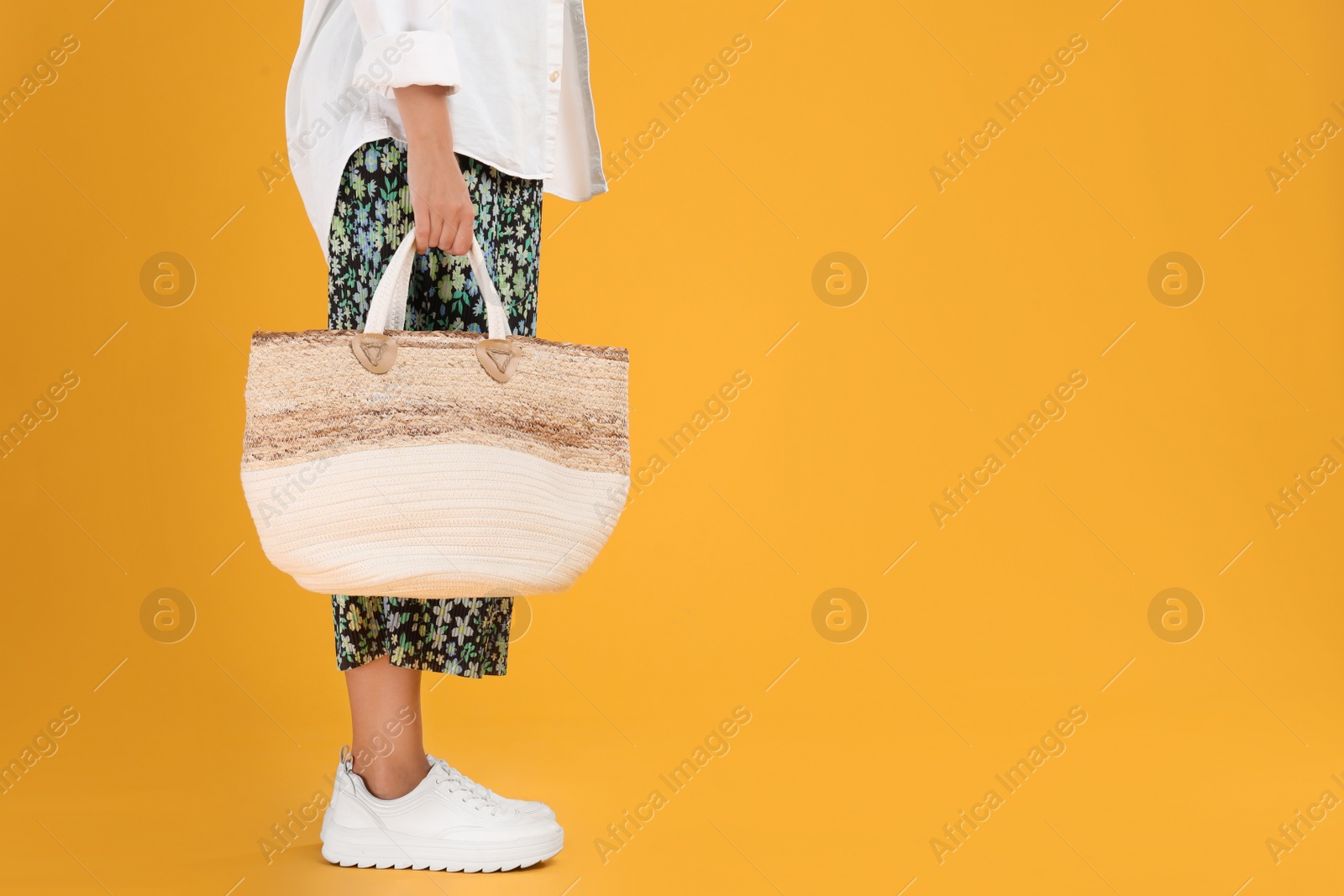 Photo of Young woman with stylish straw bag on yellow background, closeup. Space for text