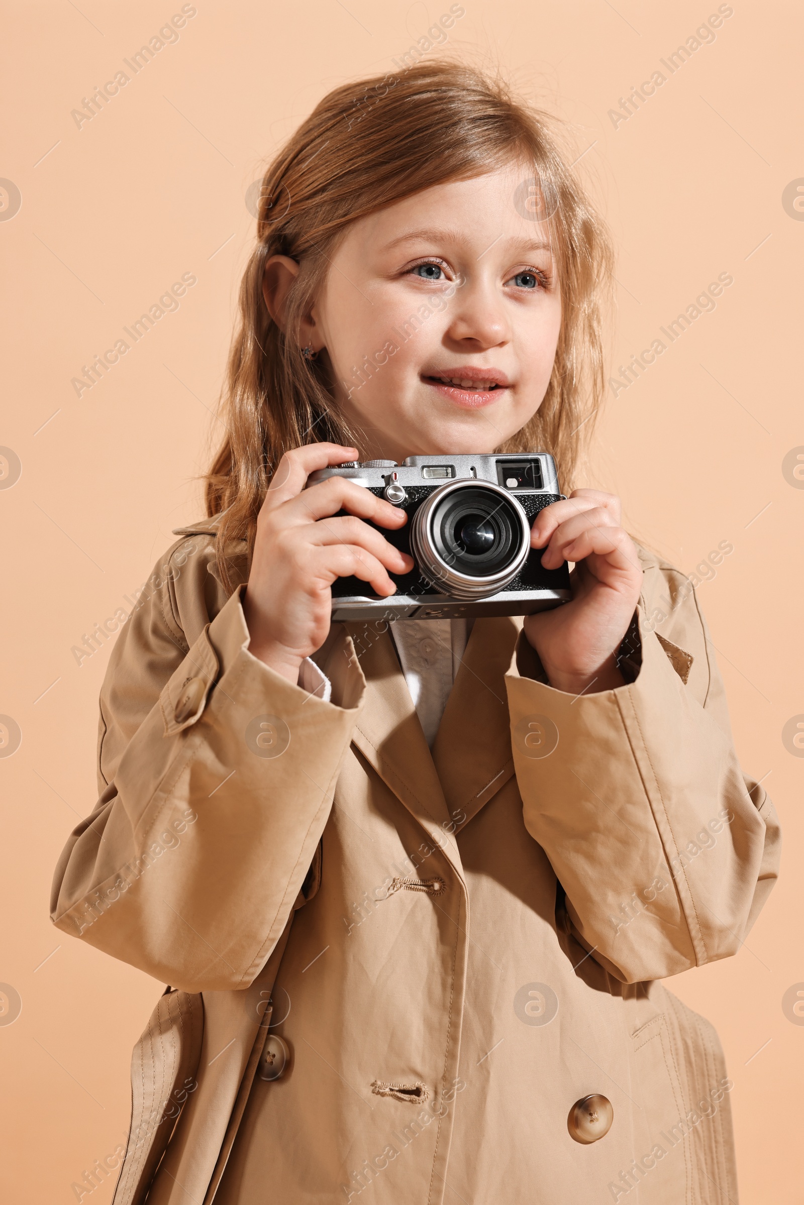 Photo of Fashion concept. Stylish girl with vintage camera on pale orange background