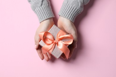 Photo of Christmas present. Woman holding gift box on pink background, top view