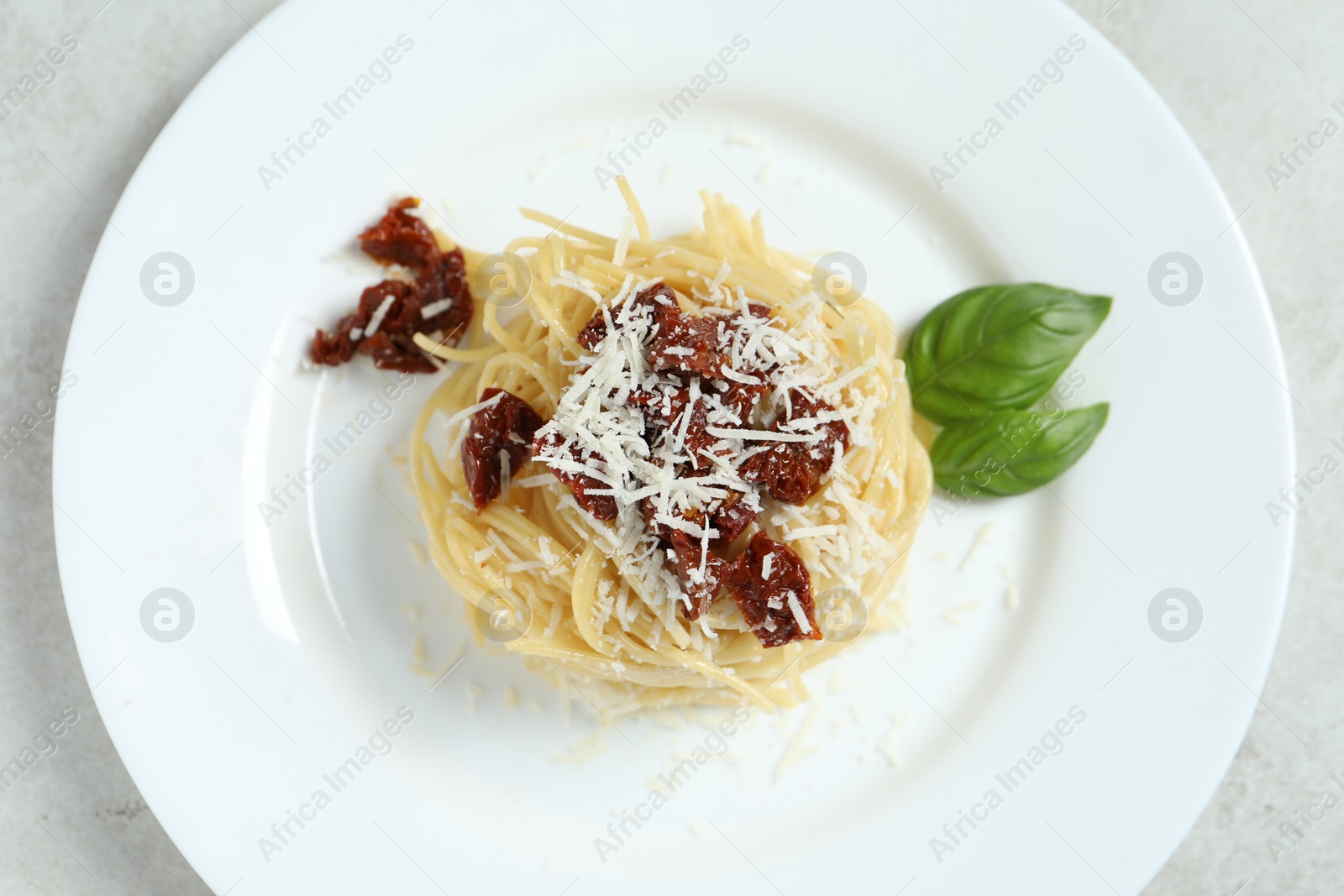 Photo of Tasty spaghetti with sun-dried tomatoes and parmesan cheese on white table, top view. Exquisite presentation of pasta dish