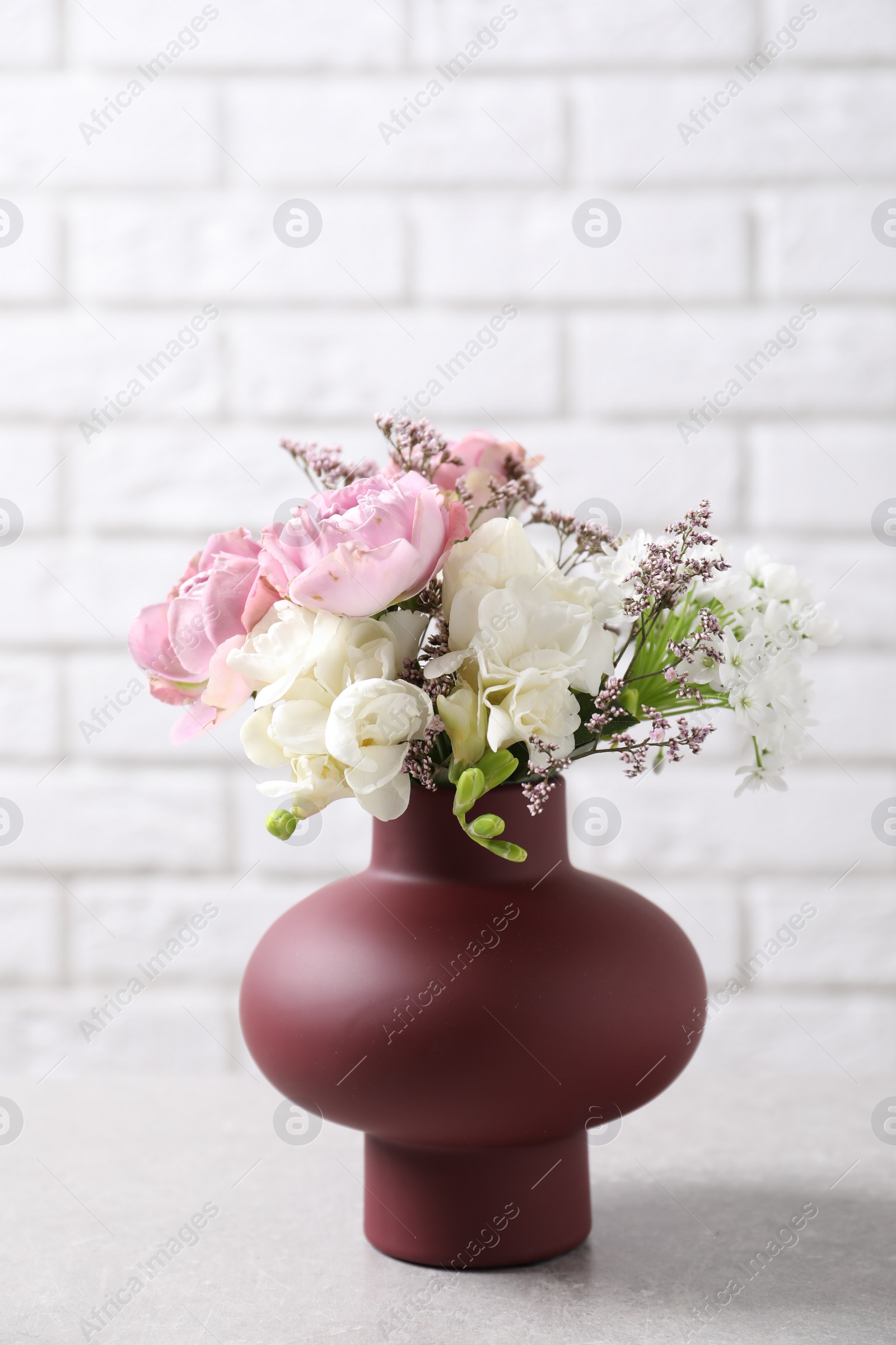 Photo of Beautiful bouquet with roses on light table against white brick wall