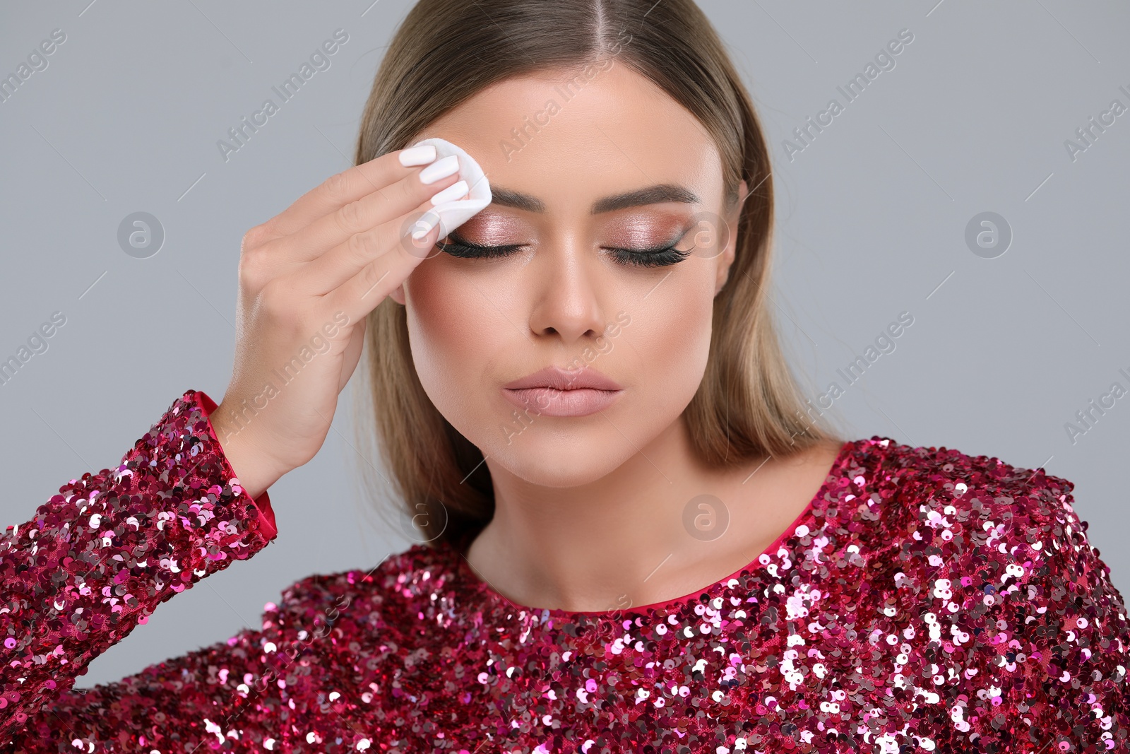 Photo of Beautiful woman removing makeup with cotton pad on grey background