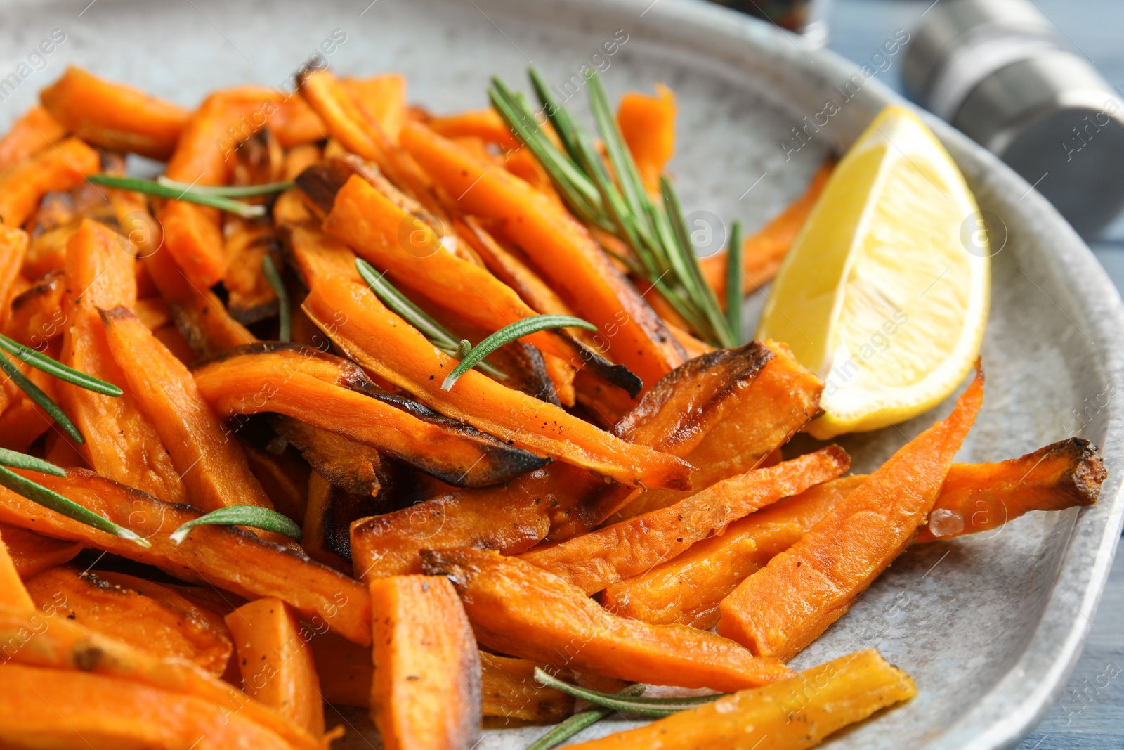 Photo of Plate with baked sweet potato slices, rosemary and lemon, closeup