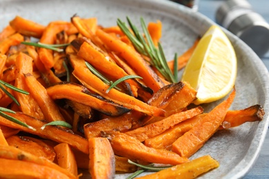 Plate with baked sweet potato slices, rosemary and lemon, closeup