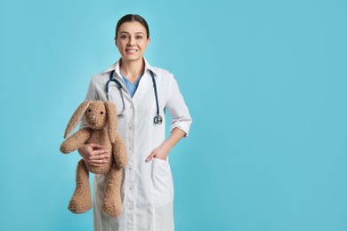 Photo of Pediatrician with toy bunny and stethoscope on turquoise background, space for text