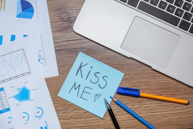 Photo of Flat lay composition of sticky note with phrase Kiss Me and heart on wooden office table