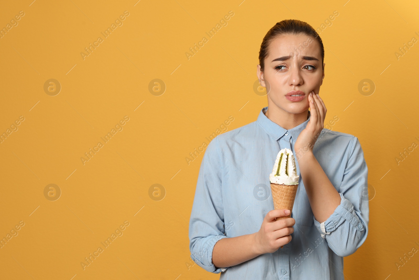 Photo of Emotional young woman with sensitive teeth and ice cream on color background. Space for text