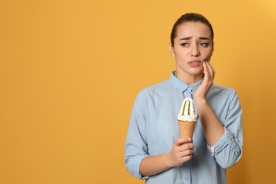 Photo of Emotional young woman with sensitive teeth and ice cream on color background. Space for text