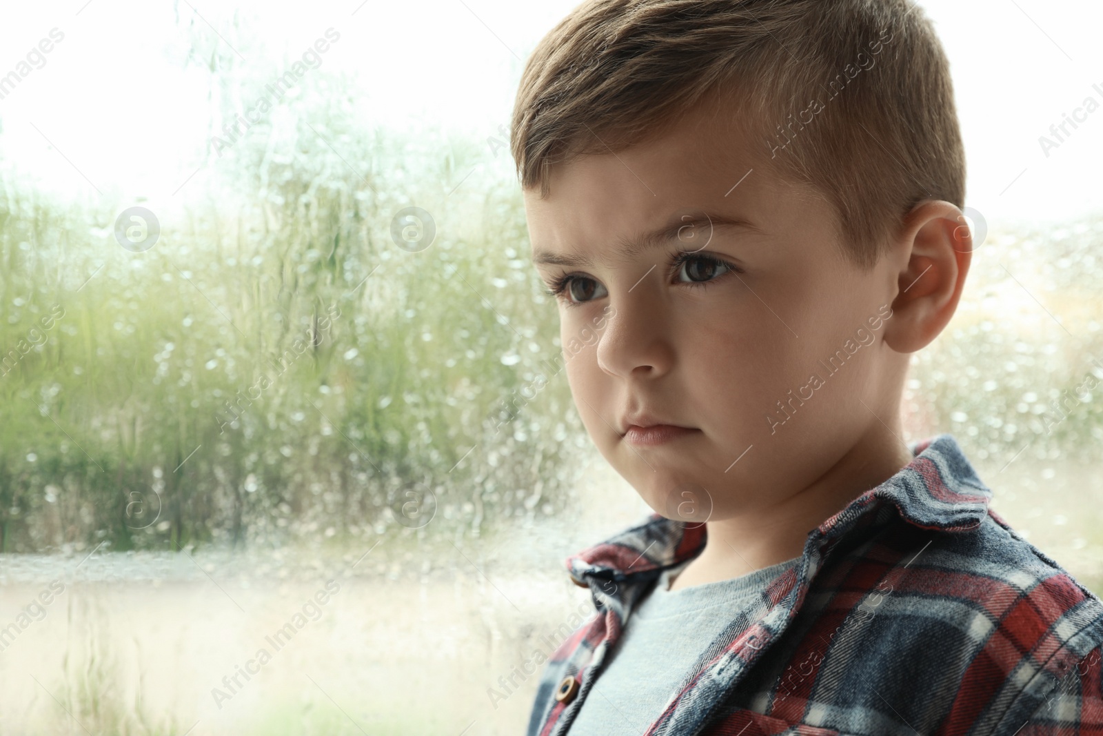 Photo of Cute little boy near window indoors, space for text. Rainy day