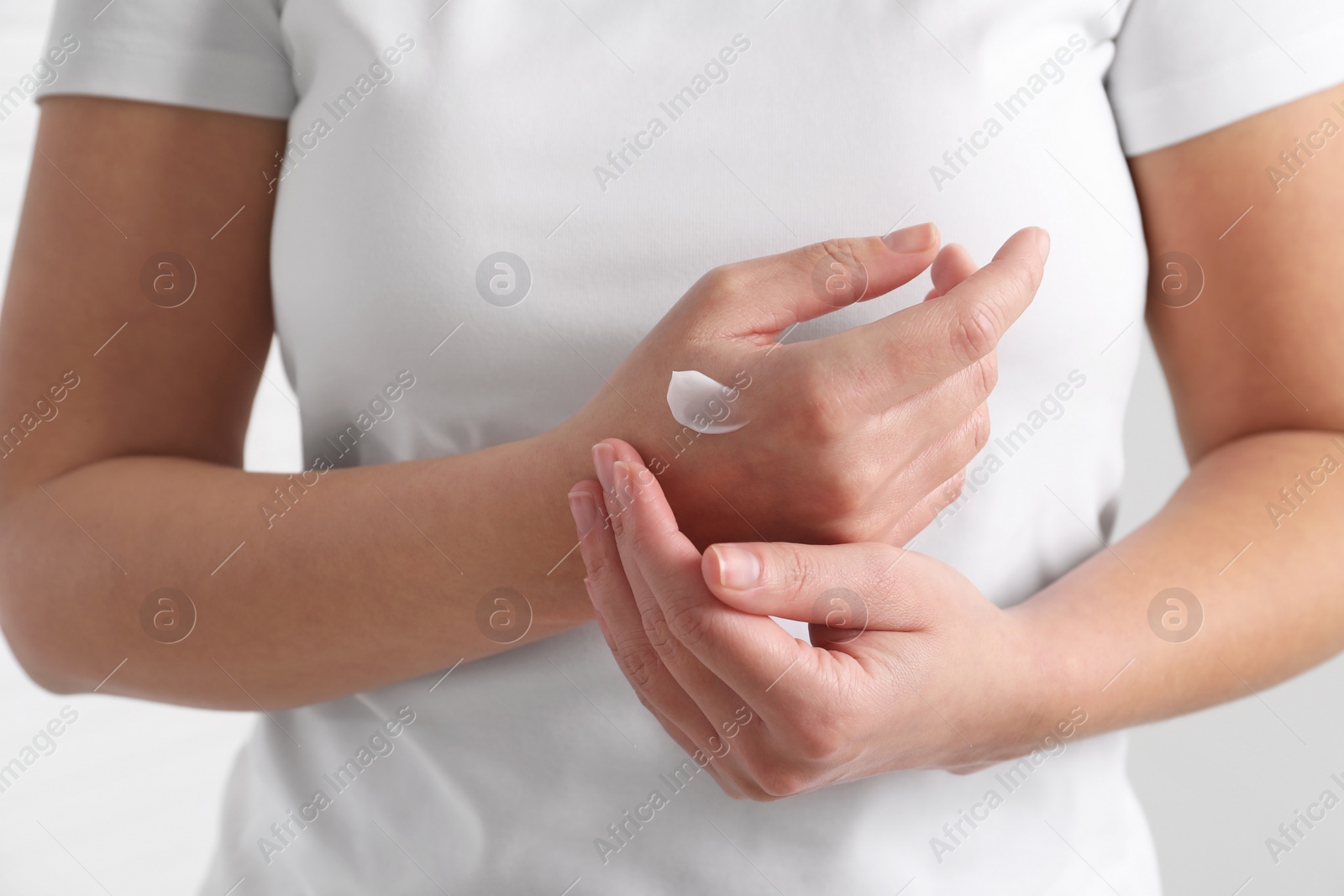 Photo of Woman applying cosmetic cream onto hand on blurred background, closeup