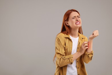 Suffering from allergy. Young woman scratching her arm on grey background, space for text