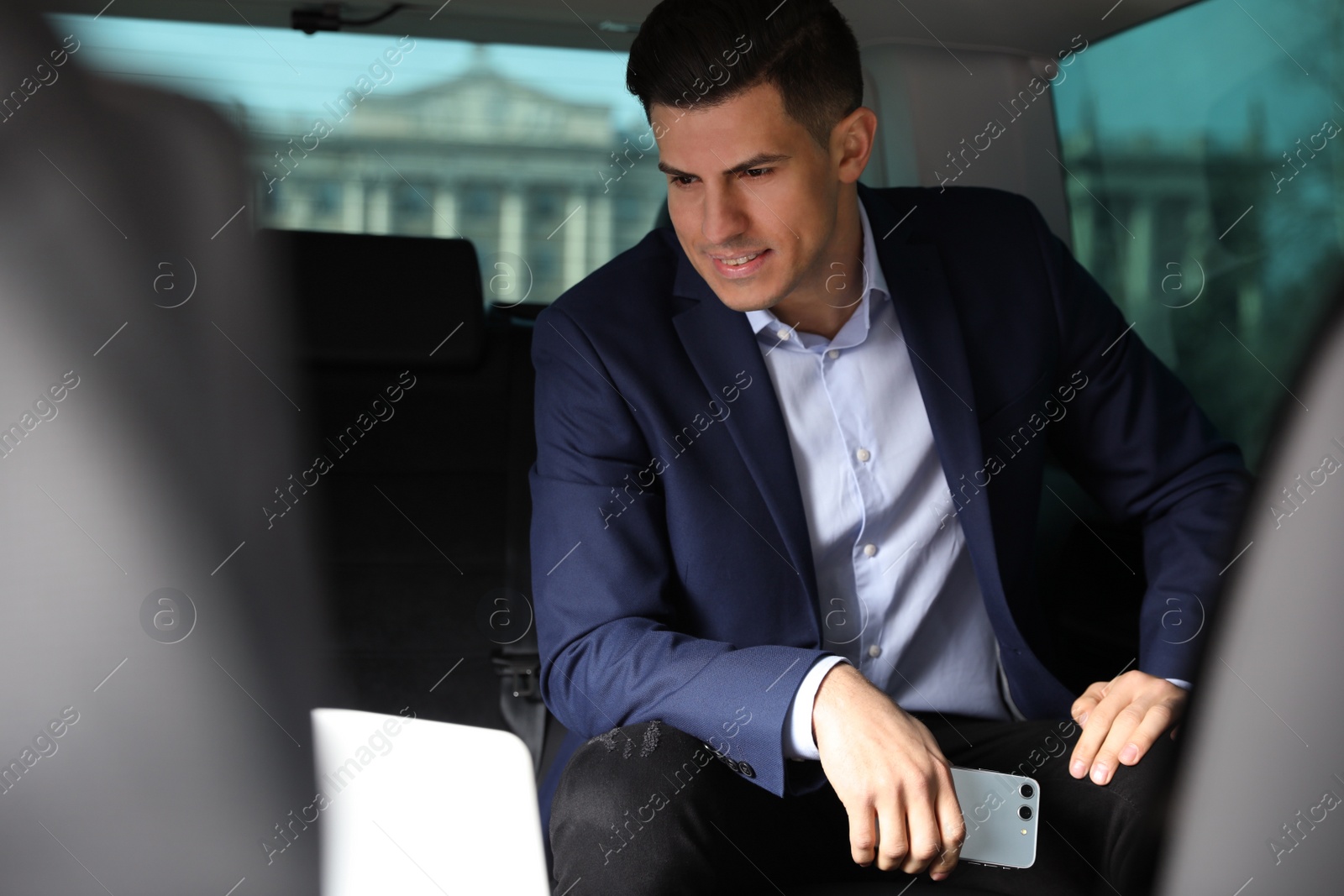 Photo of Handsome man with smartphone on backseat of modern car