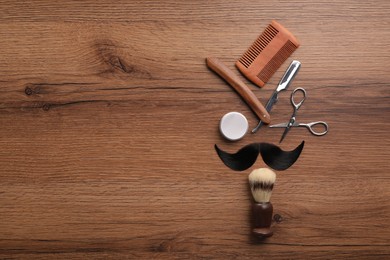 Photo of Artificial moustache and barber tools on wooden table, flat lay. Space for text