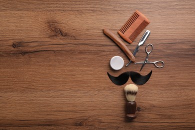 Artificial moustache and barber tools on wooden table, flat lay. Space for text