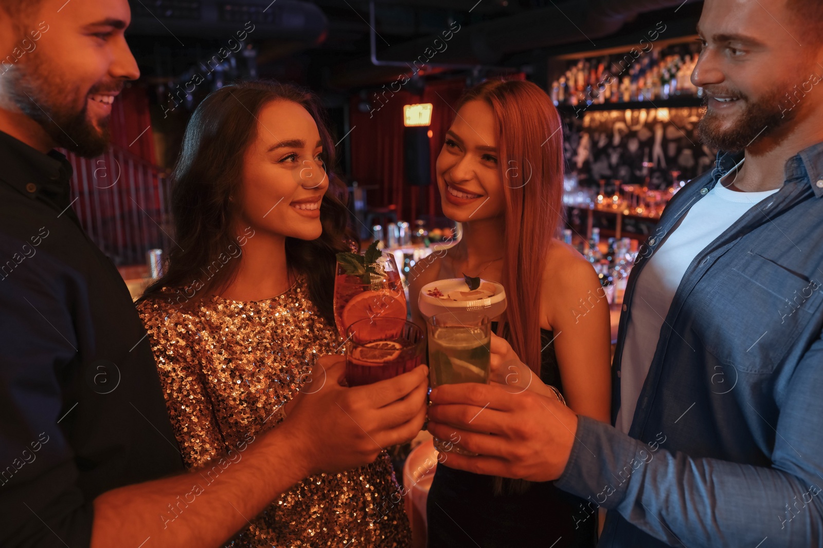 Photo of Happy friends clinking glasses with fresh cocktails in bar