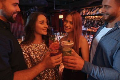 Photo of Happy friends clinking glasses with fresh cocktails in bar