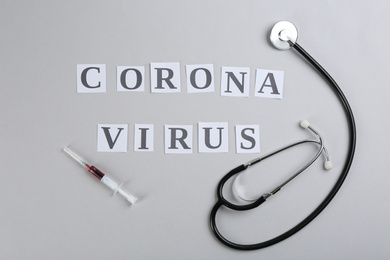 Flat lay composition with words CORONA VIRUS, stethoscope and syringe on light grey background