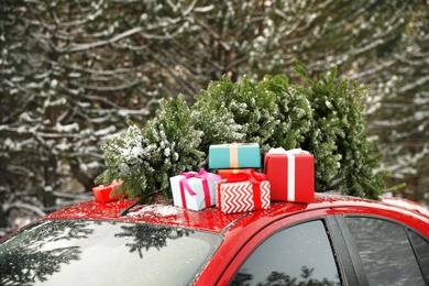 Photo of Car with Christmas tree and gifts on roof in winter forest, closeup