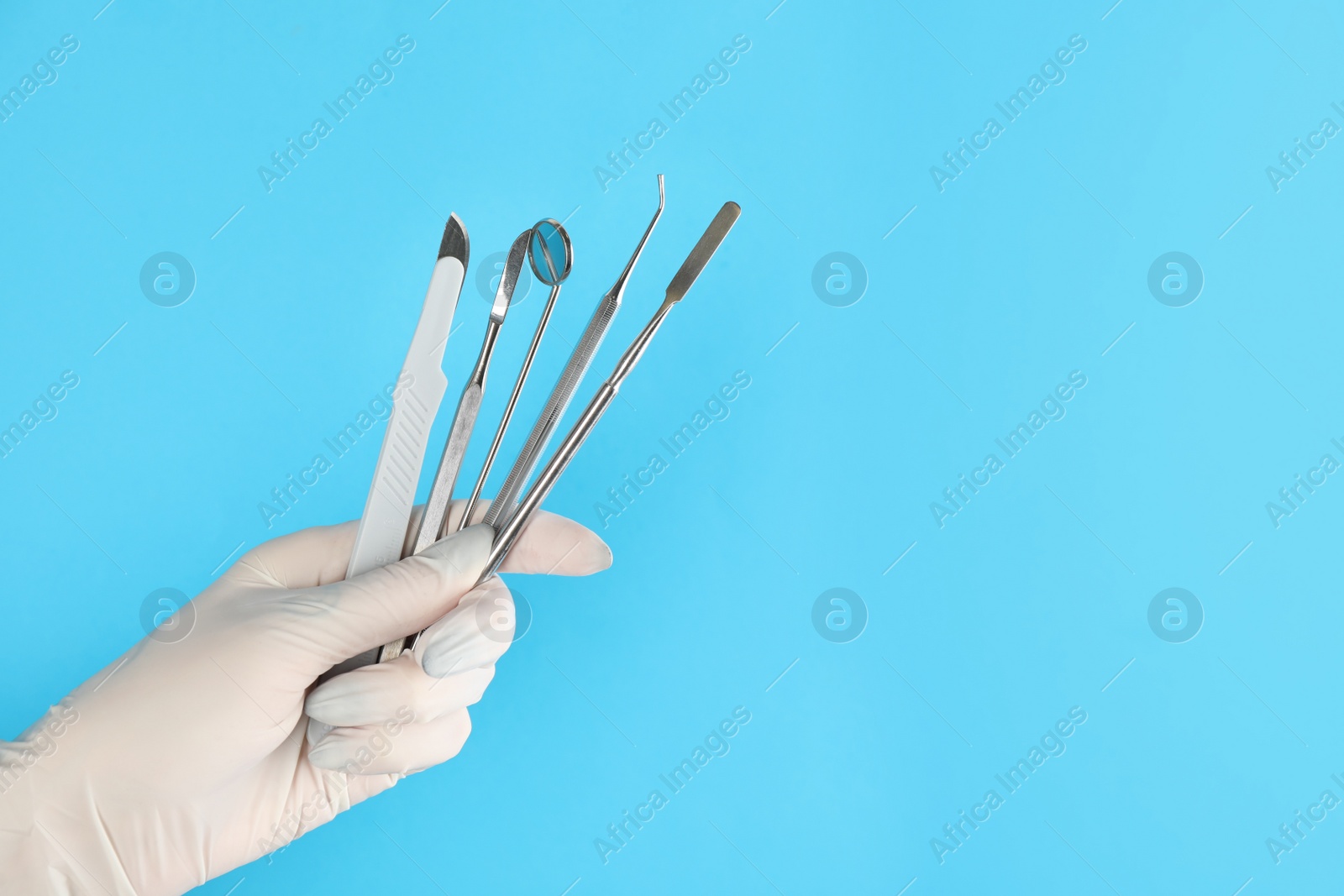 Photo of Dentist holding set of tools on light blue background, closeup. Space for text