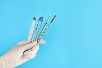 Photo of Dentist holding set of tools on light blue background, closeup. Space for text