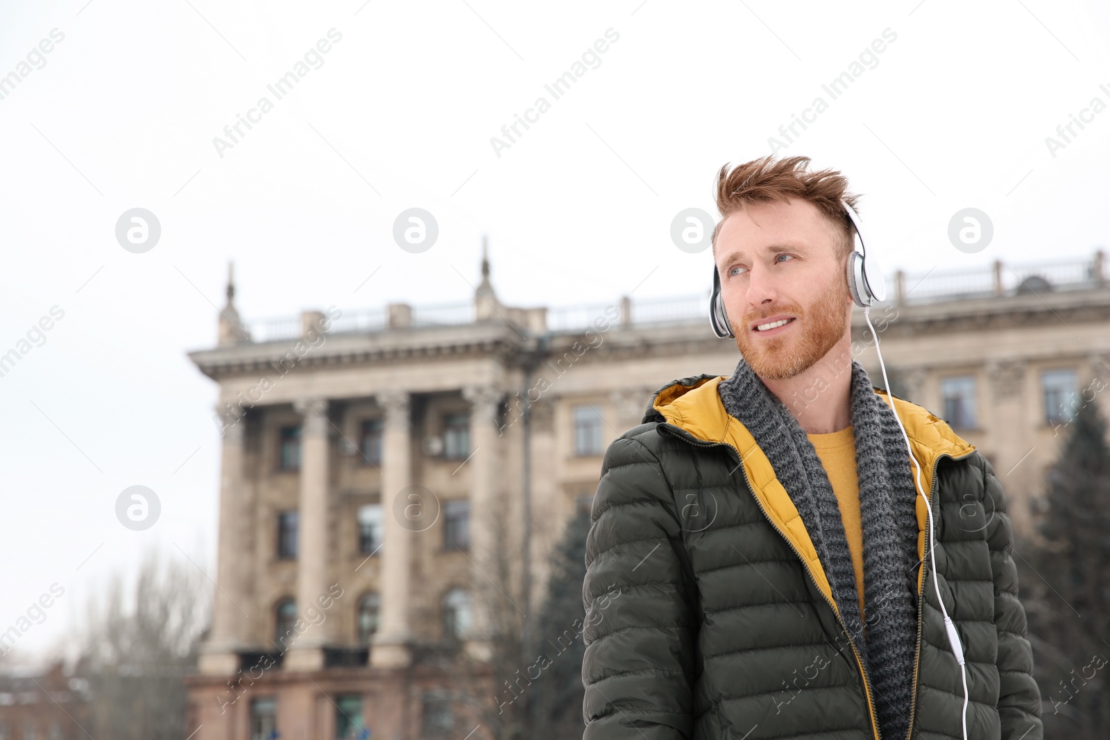 Photo of Young man listening to music with headphones outdoors. Space for text