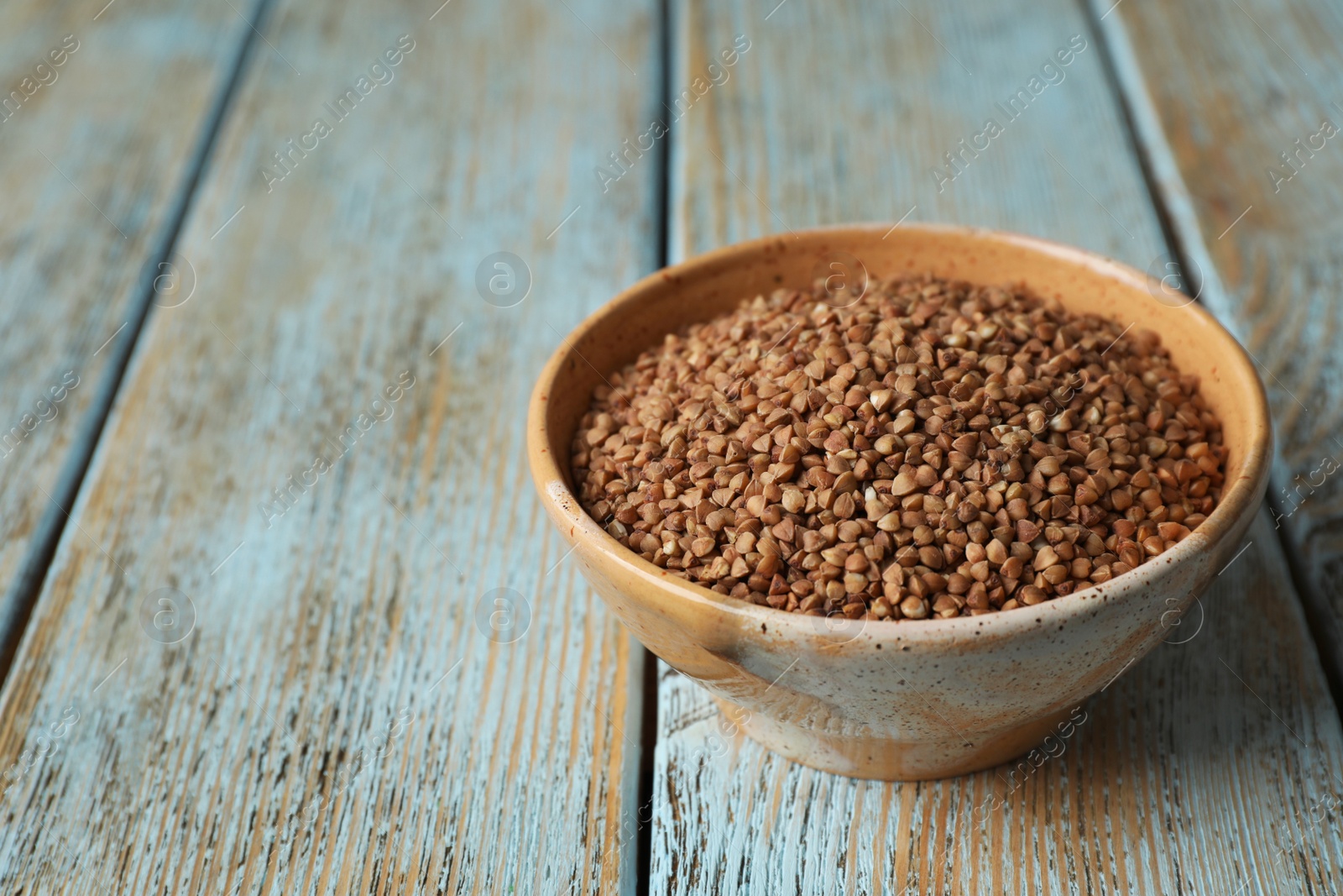 Photo of Uncooked buckwheat in bowl on table. Space for text