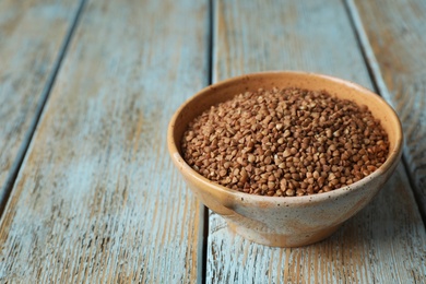 Uncooked buckwheat in bowl on table. Space for text