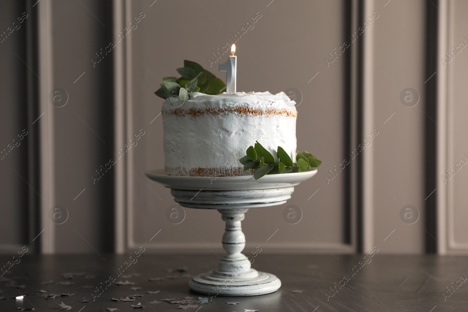 Photo of Tasty Birthday cake with burning candle and eucalyptus branches on grey table