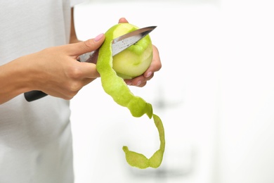 Woman peeling fresh green apple indoors, closeup. Space for text