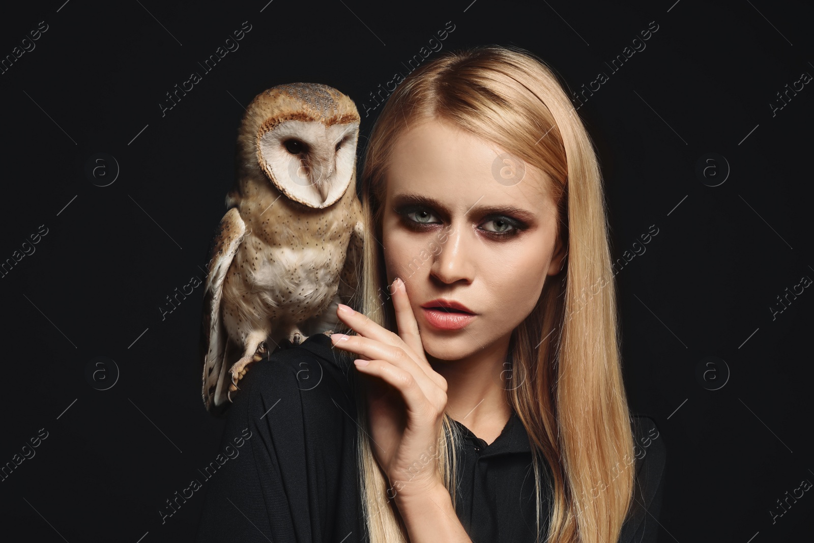 Photo of Witch in black mantle with owl on dark background. Scary fantasy character