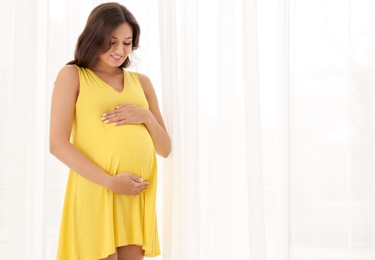 Beautiful pregnant woman near window at home