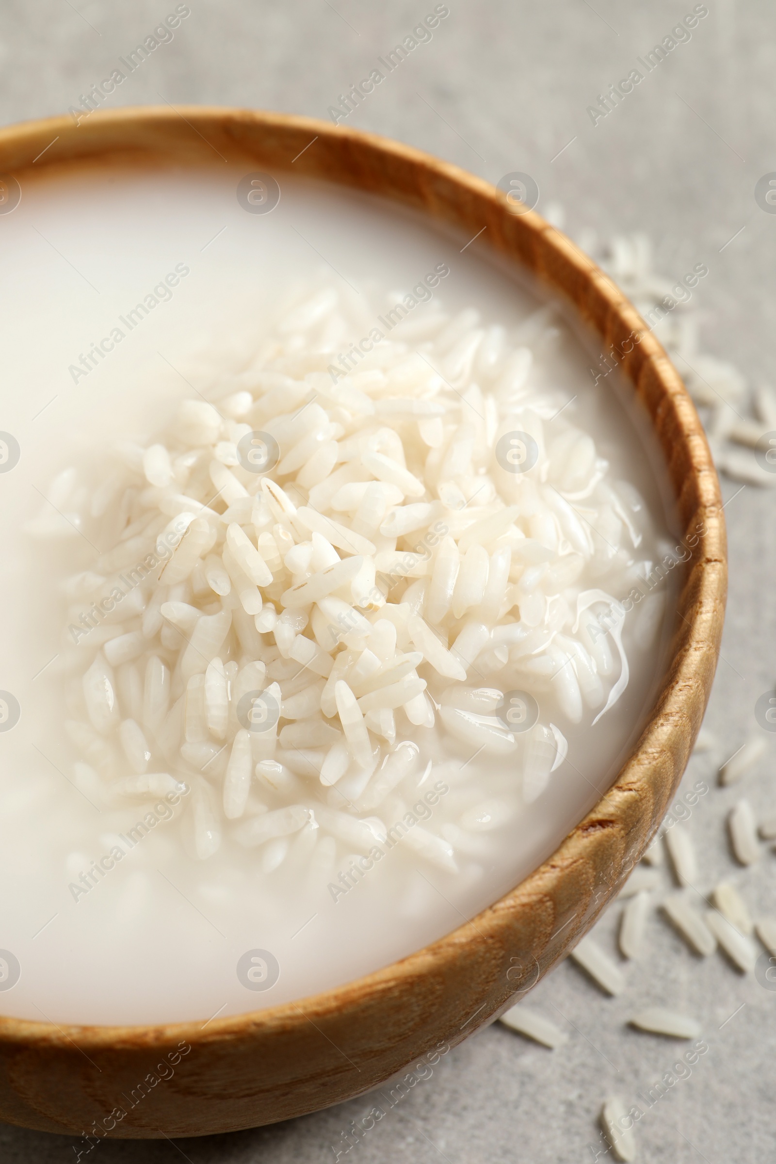 Photo of Rice soaked in water on light grey table, closeup