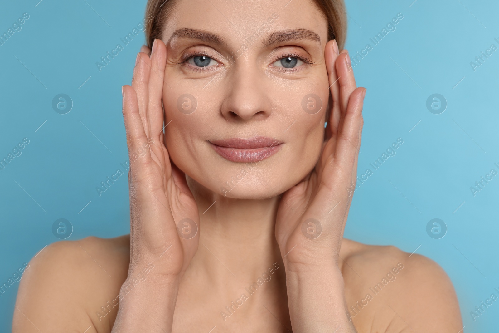 Photo of Woman massaging her face on turquoise background