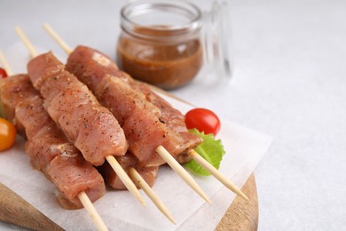 Wooden skewers with cut raw marinated meat on light grey table, closeup