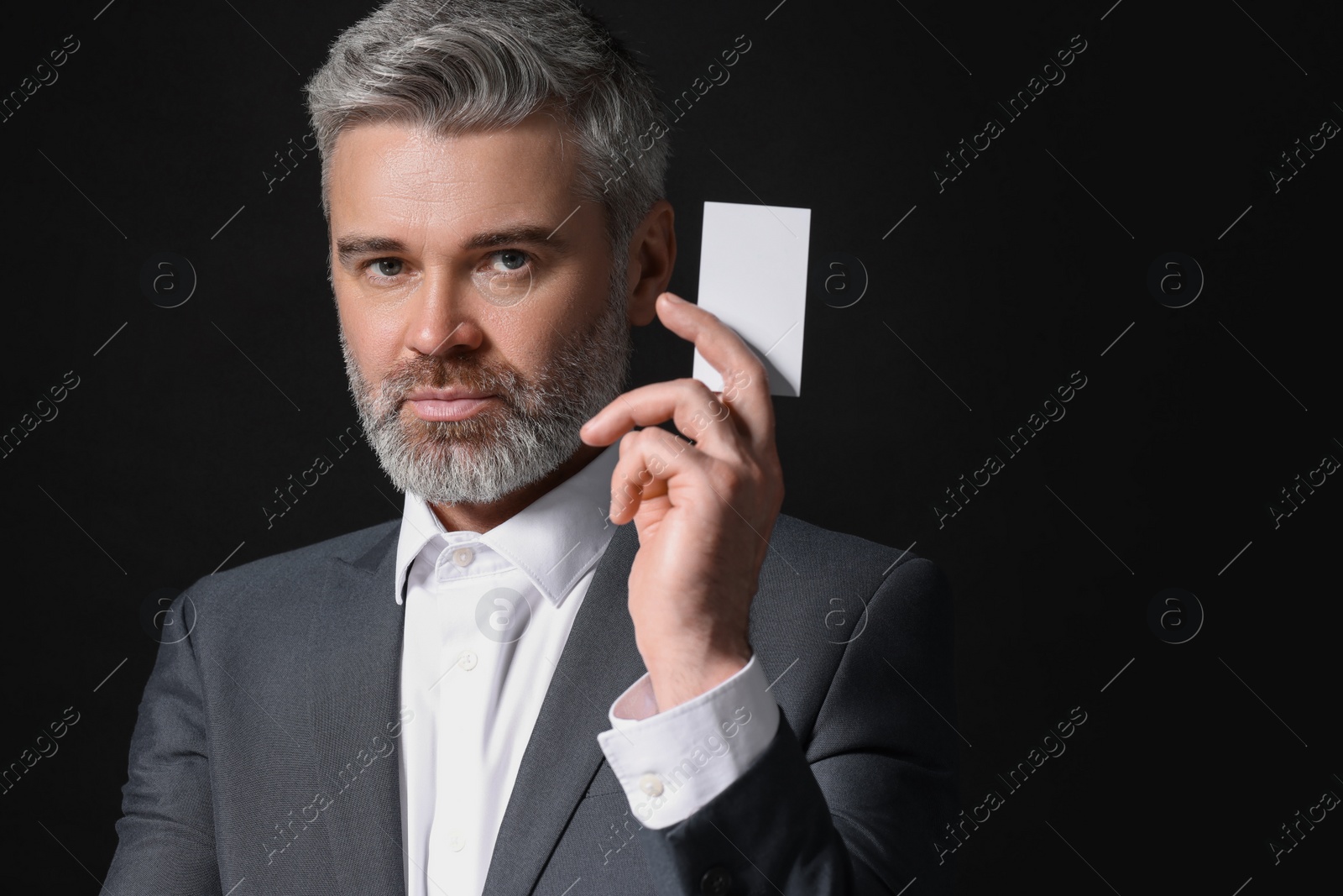 Photo of Handsome businessman holding blank business card on black background