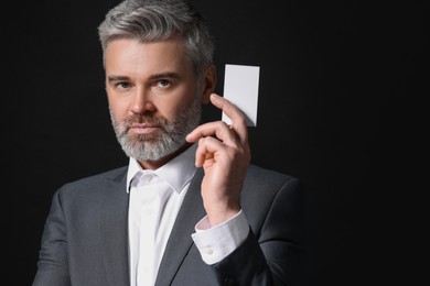 Handsome businessman holding blank business card on black background