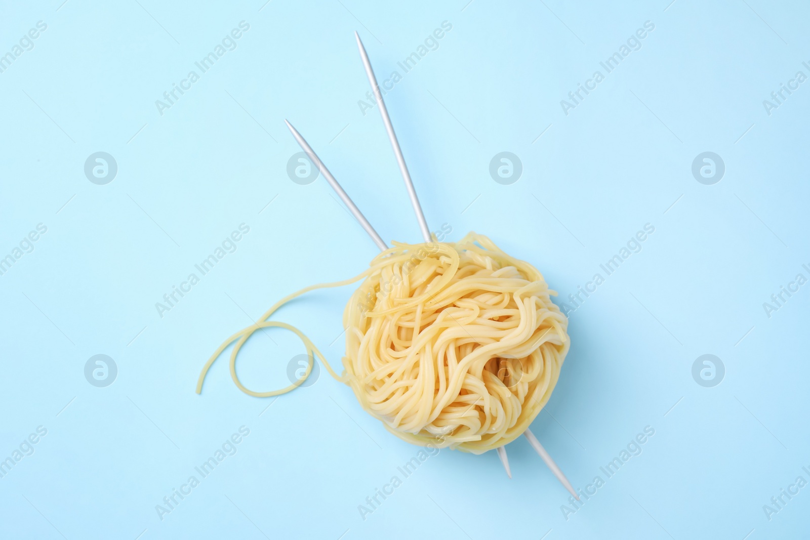 Photo of Pasta as clew with knitting needles on light blue background, top view