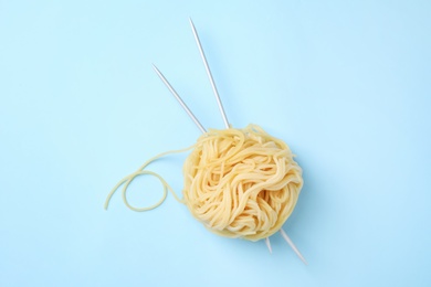 Pasta as clew with knitting needles on light blue background, top view